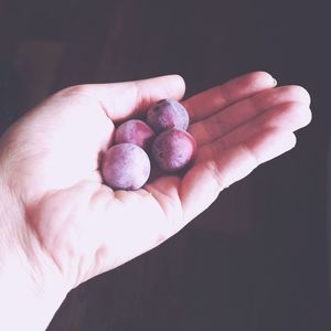 Close-up of hand holding fruits against black background