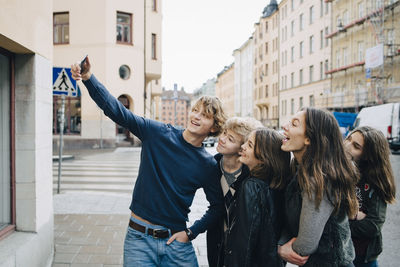 Male taking selfie with friends through smart phone while standing in city