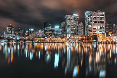 Illuminated buildings by river against sky at night