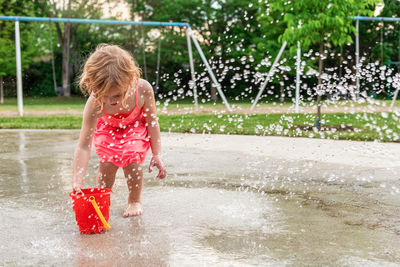 Little child playing with water and toys at splash pad in the local public park playground in summer