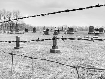 Barbed wire fence on field against sky