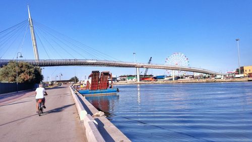 People on bridge over river against clear blue sky