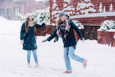 Two young women play snowballs and laugh while walking through a snowy town