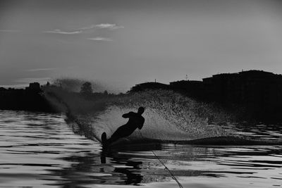 Silhouette man waterskiing on lake against sky