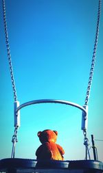 Teddy bear on swing against sky