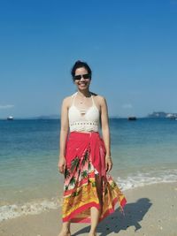 Portrait of woman standing at beach against clear blue sky