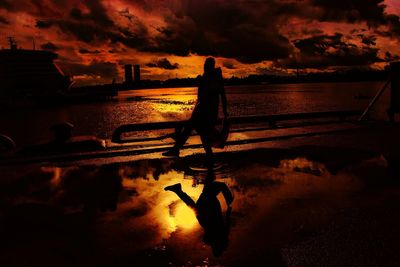 Silhouette man standing in sea against sky during sunset