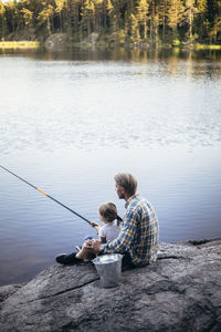 Father and daughter fishing while sitting by lake