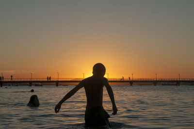 Silhouette people standing by sea against orange sky