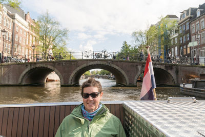 Portrait of woman sitting on boat in canal against bridge in city