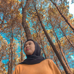 Low angle view of young woman wearing hijab against trees in forest