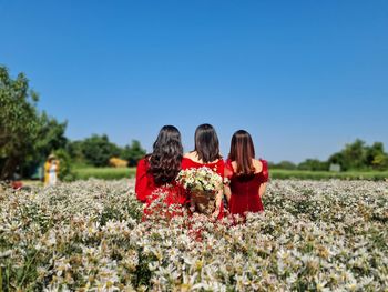 Rear view of women with flowers against clear sky