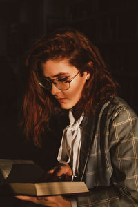 Young woman reading book against black background