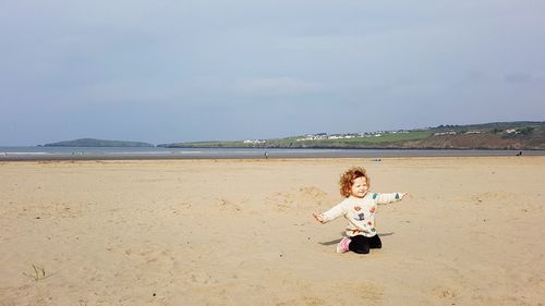 Full length of woman sitting on beach against sky