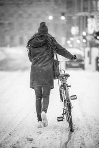 Rear view of person walking with bicycle on road in winter