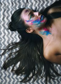 Directly above shot of shirtless woman with face paint lying on bed