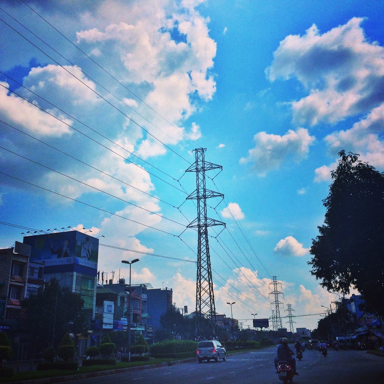 sky, building exterior, cloud - sky, electricity pylon, transportation, power line, built structure, architecture, car, cloud, mode of transport, cloudy, electricity, land vehicle, street, blue, city, road, power supply, cable