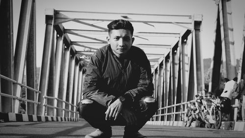 Portrait of young man crouching on bridge