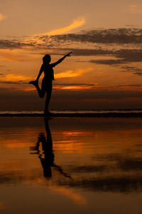 Silhouette woman standing at beach against sky during sunset