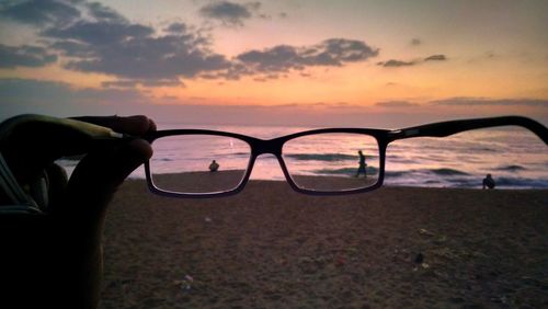 Close-up of eyeglasses on beach against sky during sunset
