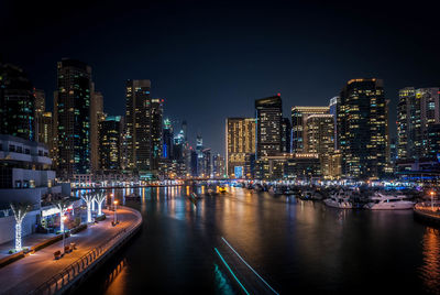 Boats moored at marina by illuminated cityscape at night