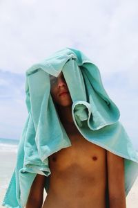 Portrait of shirtless teenage boy standing with towel on head at beach