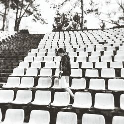 Woman walking amidst chairs against trees