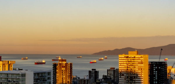 Sea by buildings against sky during sunset