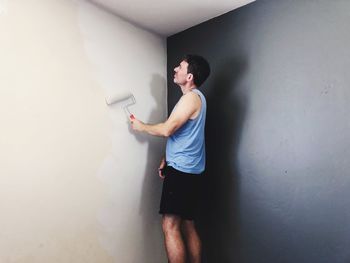 Side view of young man standing against wall at home