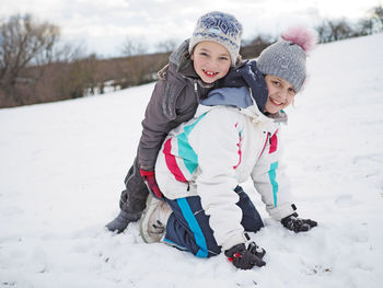 Portrait of playful siblings playing on snow during winter