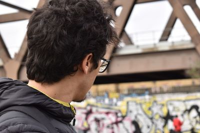 Close-up of man looking away while standing against bridge