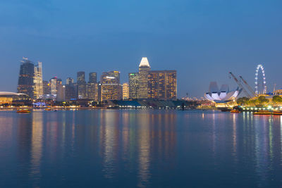 Illuminated city by river against sky