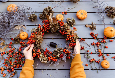 Girl making floral autumn door wreath using colorful rosehip berries, rowan, dry flowers and pumpkin