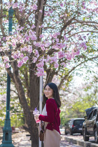 Rear view portrait of woman standing by pink flowering tree