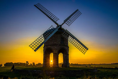 Traditional windmill on field against sky during sunset