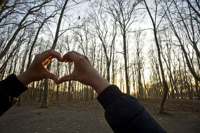 Midsection of couple kissing heart shape against trees