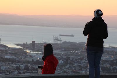 Rear view of woman looking at cityscape against sky during sunset