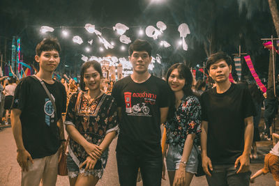 Portrait of friends standing against illuminated people at night