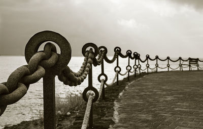 Fence by sea against cloudy sky at dusk
