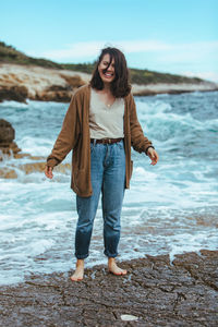 Young woman standing at beach against sky