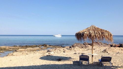 Parasol and lounge chairs at beach against clear sky 