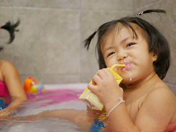 Portrait of shirtless girl drinking while sitting in bathtub