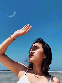 Young woman shielding eyes against blue sky