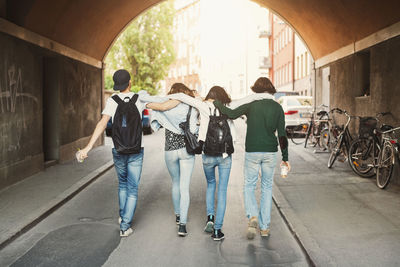 Rear view of teenagers with arms around walking in tunnel