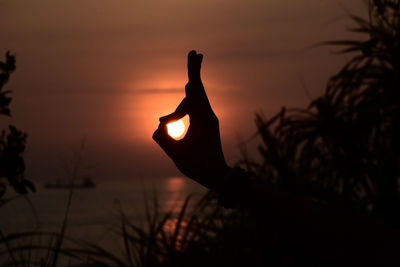 Optical illusion of silhouette hand holding sun at beach during sunset