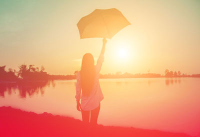 Silhouette woman standing by lake against sky during sunset