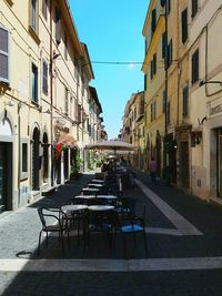 Chairs and tables on street in city against sky