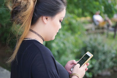 Side view of woman text messaging mobile phone while standing at park