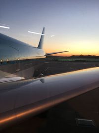 Airplane on airport runway against sky during sunset