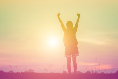 Rear view of silhouette woman standing on field against sky during sunset